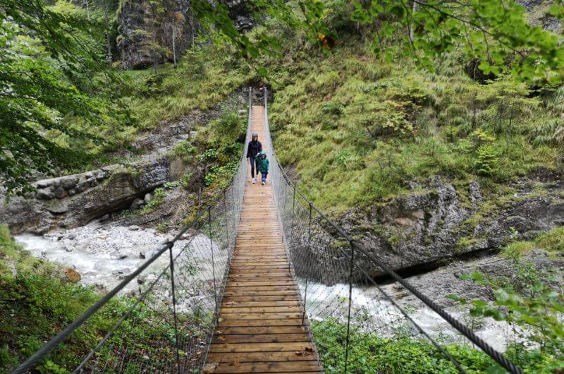 Mama und Kind wandern über eine Hängebrücke über die Grießbachklamm in Tirol.