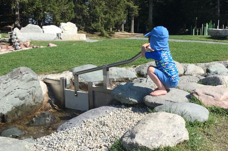 Kind am kinderfreundlichen Wasserspielplatz Timoks Wilde Welt in Fieberbrunn im Urlaub mit Kindern in Tirol.